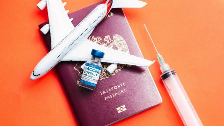 Photo d'un passeport rouge sur lequel sont posés : avion miniature, fiole de vaccin et seringue